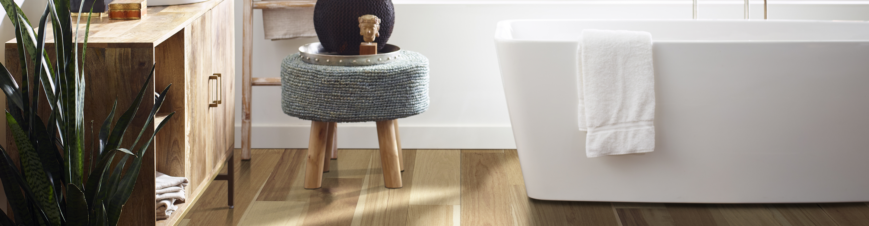 Natural light hardwood flooring in bathroom with white soaker tub and grey footstool