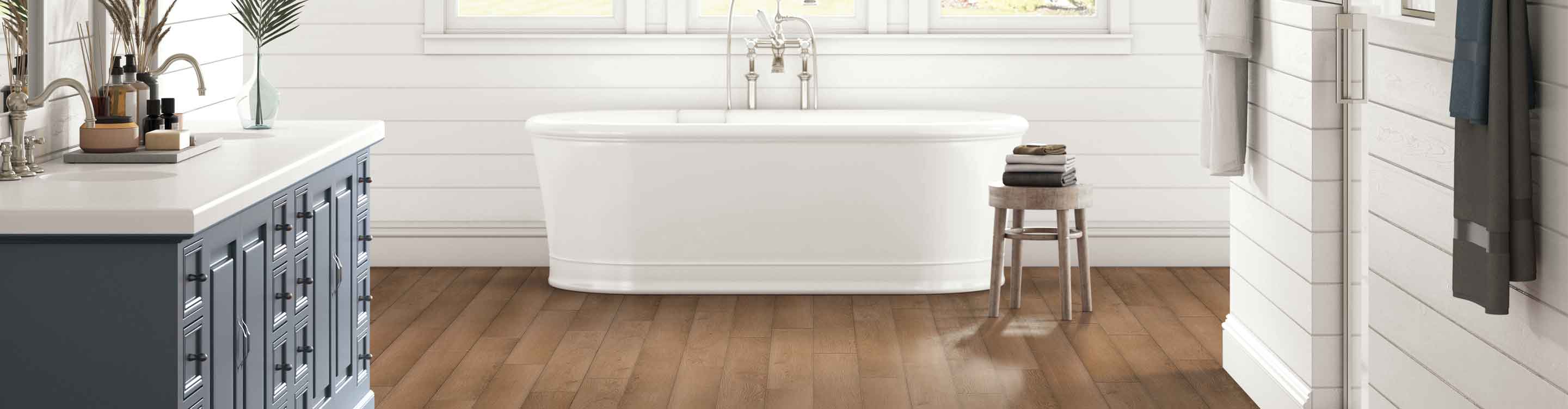 honey-hued wood-look vinyl flooring in modern bathroom with shiplap walls, deep soak tub and blue vanity
